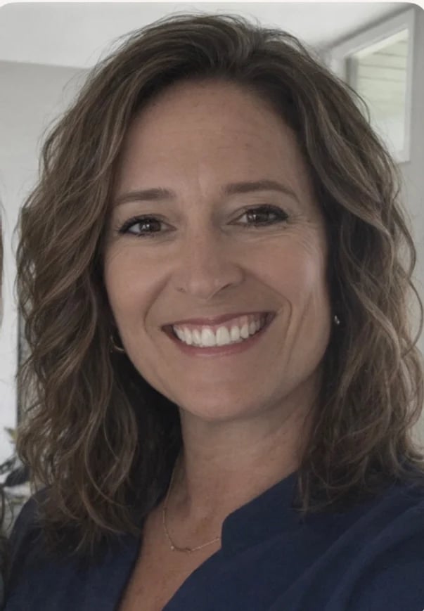 Portrait of a smiling woman with shoulder-length wavy brown hair wearing a dark navy top